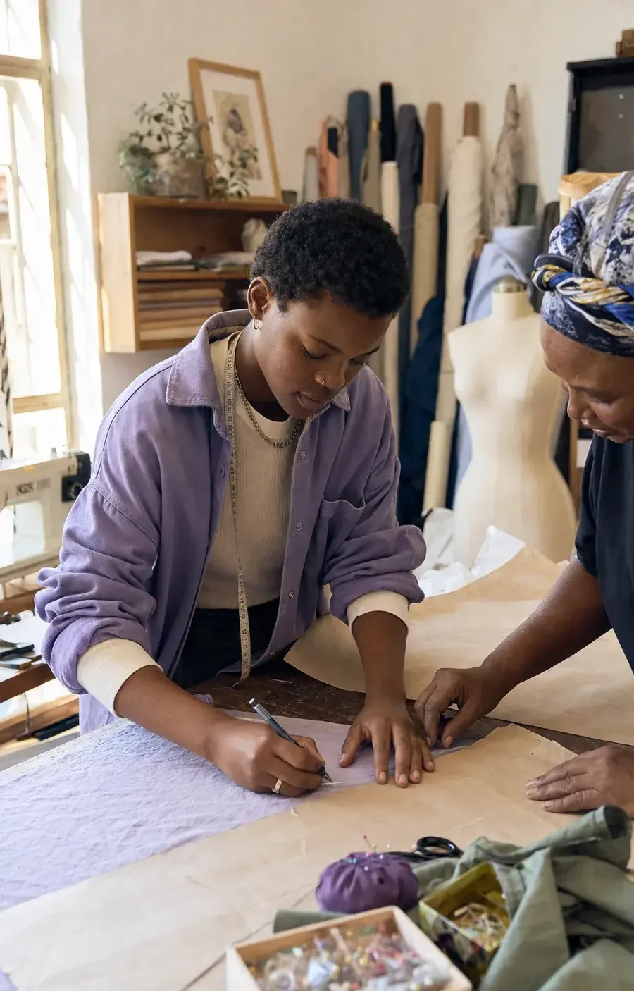 A young designer marks up a fabric pattern while a mentor looks on